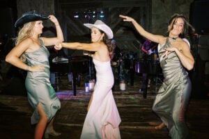 Three women at a Texas wedding dance as a dueling piano band provides a lively wedding entertainment option in the background.